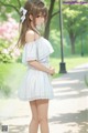 A girl in a white dress standing in a park.