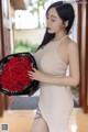 a woman in a beige dress holding a bouquet of red roses