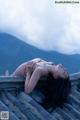 A woman laying on top of a roof with mountains in the background.