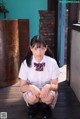 A young woman in a school uniform sitting on a wooden floor.