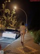 A naked woman walking down a sidewalk next to a car.