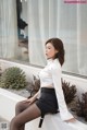 A woman in a white shirt and black skirt sitting on a ledge.