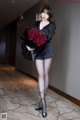 A woman in a black dress holding a bunch of red roses.