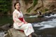 A woman in a kimono sitting on a rock by a river.