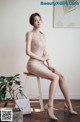 A woman sitting on a stool in a beige dress.