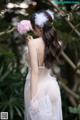 A woman in a white dress holding a pink flower.