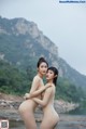 A couple of naked women standing next to each other on a beach.