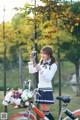 A woman in a school uniform holding a camera and a bicycle.