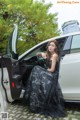 A woman in a black dress sitting in the driver's seat of a car.