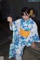 A woman in a blue and white kimono sitting on a bench.