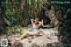 A woman in a blue bathing suit sitting on a rock.