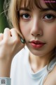 A close up of a woman's face with a green ring on her finger.