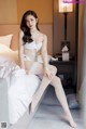 A woman sitting on a bed in a white lingerie.