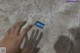 A person's hand is touching a small blue object on the floor.