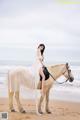 A woman in a white dress riding a horse on the beach.