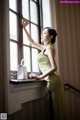 A woman in a green dress standing by a window.