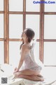 A woman sitting on a bed in a white lingerie.