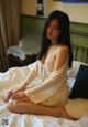 A woman sitting on a bed in a white robe.