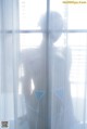 A woman standing in front of a window with sheer curtains.