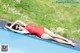 A woman in a red swimsuit laying on the edge of a swimming pool.