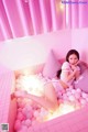 A woman laying in a pink bathtub filled with pink balls.