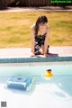 A woman sitting on the edge of a swimming pool with a rubber duck.