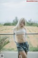 A woman in a white top and denim shorts posing for a picture.