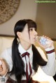 A woman in a school uniform drinking water from a bottle.