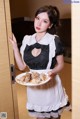 A woman in a maid outfit holding a plate of food.