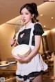 A woman in a maid outfit holding a bowl and a whisk.