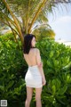 A woman in a white dress standing in front of a palm tree.