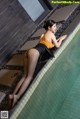 A woman in a yellow top and black skirt leaning on the edge of a pool.