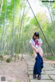 A woman in a school uniform is walking through a bamboo forest.