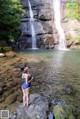 A woman in a blue bathing suit standing in front of a waterfall.