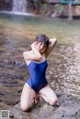 A woman in a blue bathing suit sitting on a rock by a river.