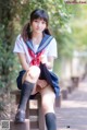 A woman in a school uniform sitting on a bench.