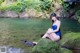 A woman in a blue bathing suit sitting on a rock by the water.