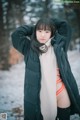 A woman in a black jacket and orange bikini standing in the snow.