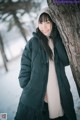 A woman leaning against a tree in the snow.