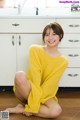 A woman in a yellow sweater sitting on the floor.