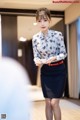 A woman in a blue and white shirt and black skirt holding a cup of coffee.