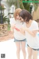 Two young women standing next to each other near a swimming pool.