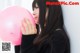 A woman holding a pink balloon in front of her face.