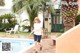 A woman in a white shirt and blue shorts walking by a pool.