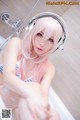 A woman with pink hair sitting in a bathtub with headphones on.