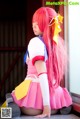 A woman with long pink hair sitting on the ground.