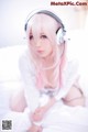 A woman with pink hair wearing headphones on a bed.