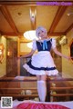 A woman in a maid outfit standing on a bed.