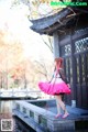 A woman in a pink dress is standing by a pond.