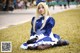 A woman in a blue and white dress sitting on the grass.